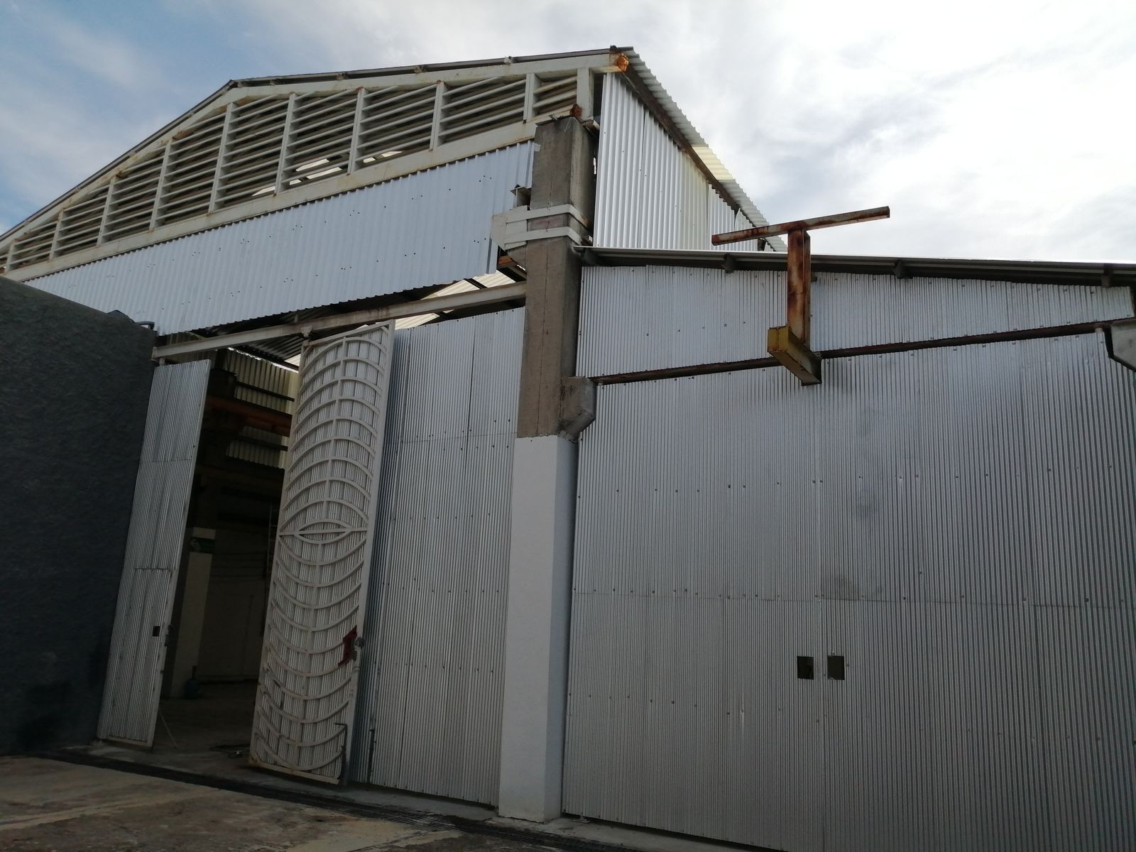 Frente de la nave principal: frontón con ventilas de persiana, portones altos de lámina y una reja de herrería abierta.