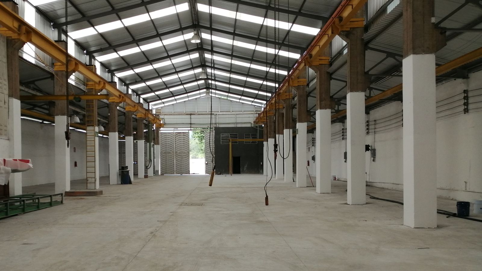 Interior de la nave principal vacía en 2021: columnas de concreto con la base pintada de blanco, las trabes amarillas de la grúa viajera a los dos lados y la cubierta con franjas translúcidas.