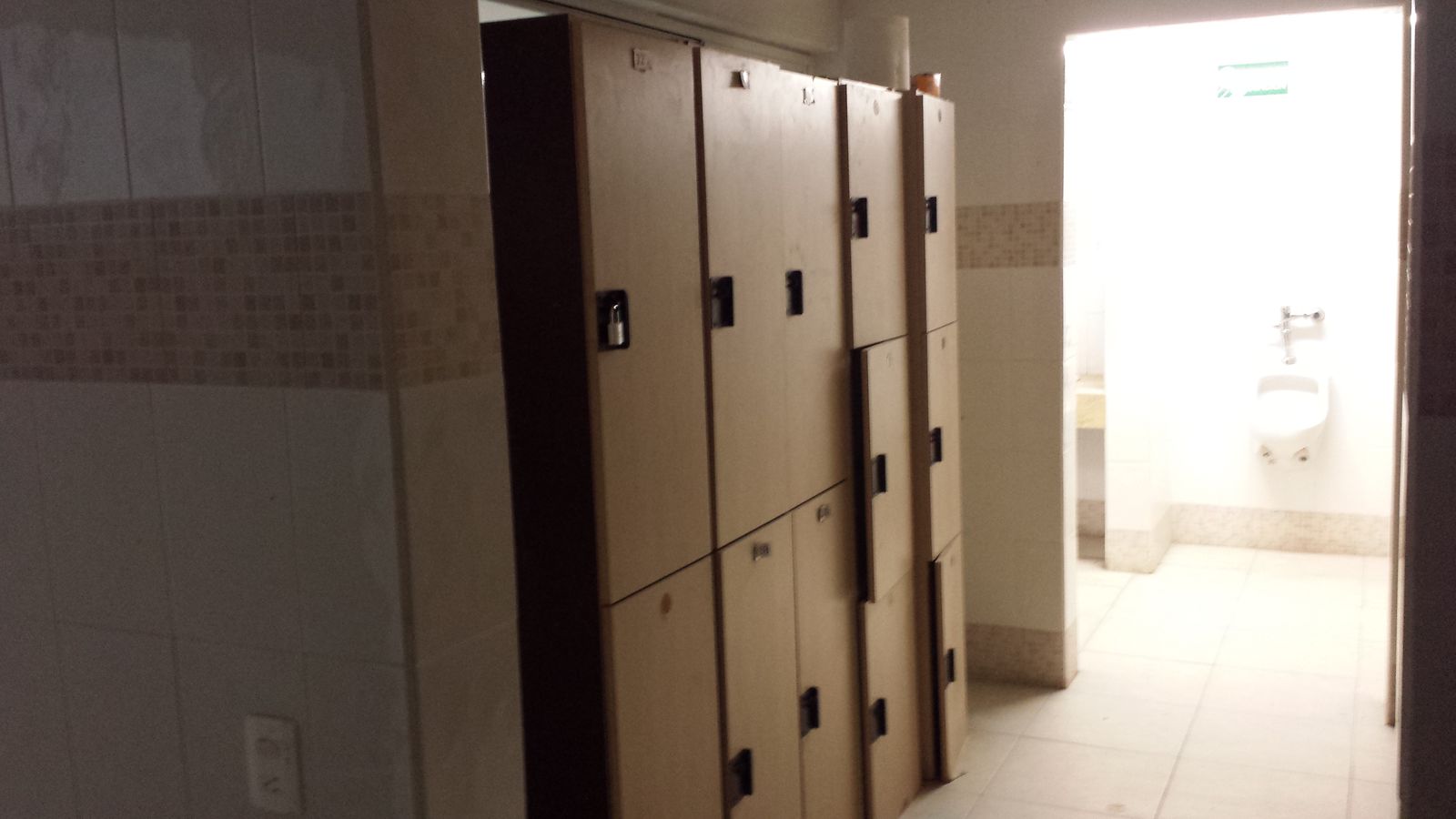 Vestidores del personal con lockers y, al fondo, el baño con mingitorio y muros de azulejo.